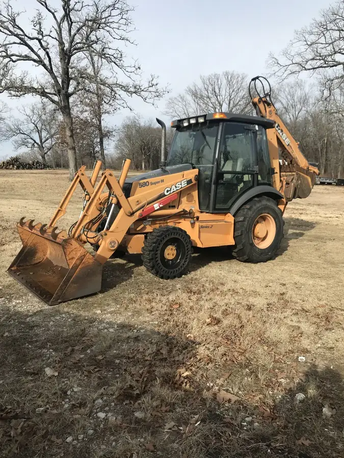 A yellow backhoe parked on a rural lot ready to dig