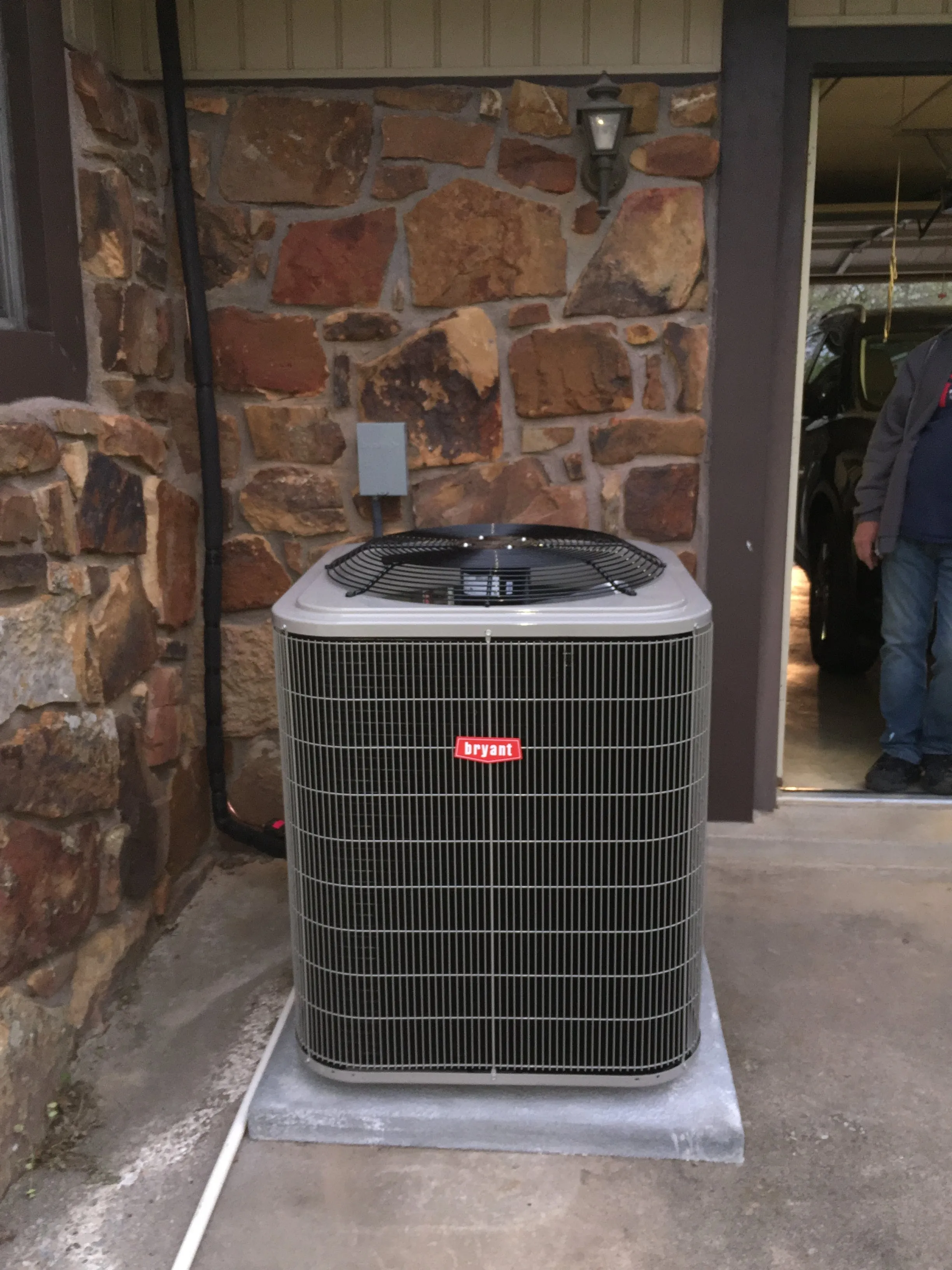 A new Bryant AC condenser installed on a concrete pad beside a stone house