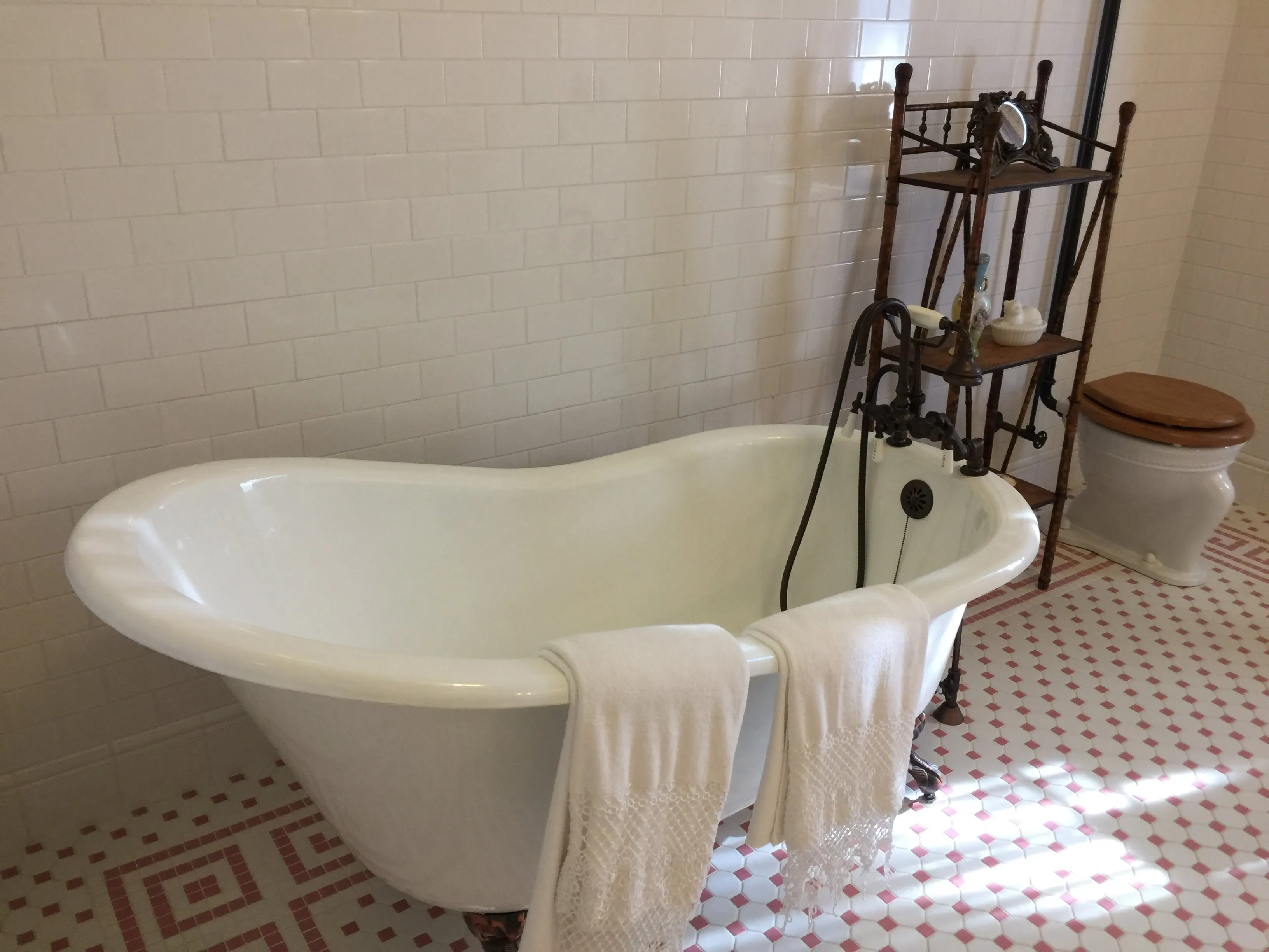 A clawfoot slipper tub with oil-rubbed bronze fixtures in a bathroom with subway tile and mosaic floor
