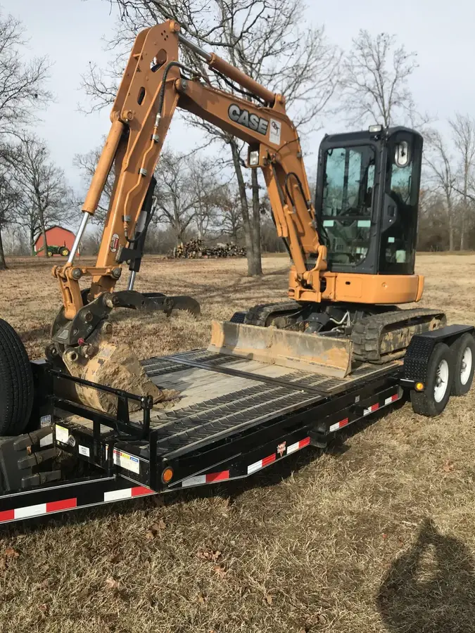 An orange mini excavator on a trailer on a rural lot