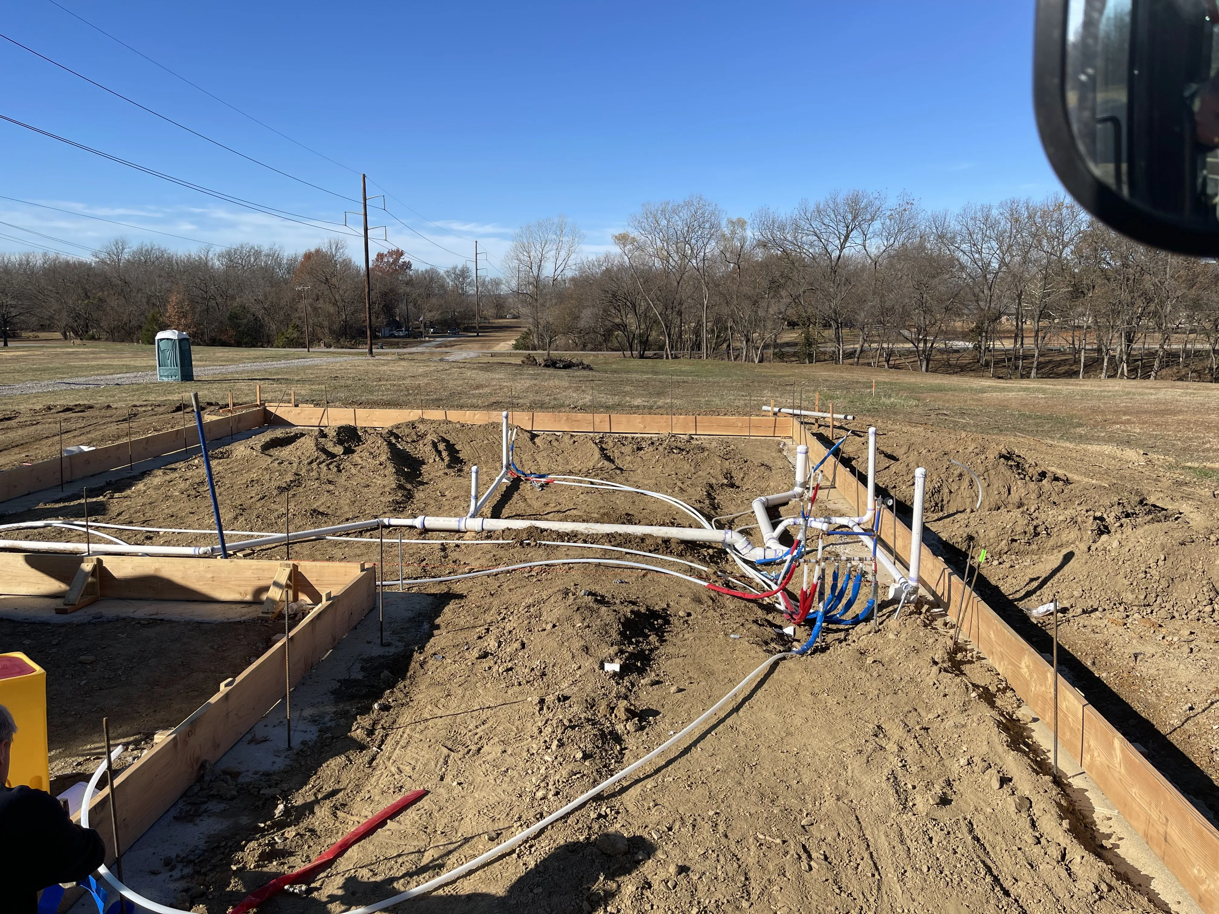 Foundation plumbing rough-in on a clear day with PEX and PVC lines inside form boards
