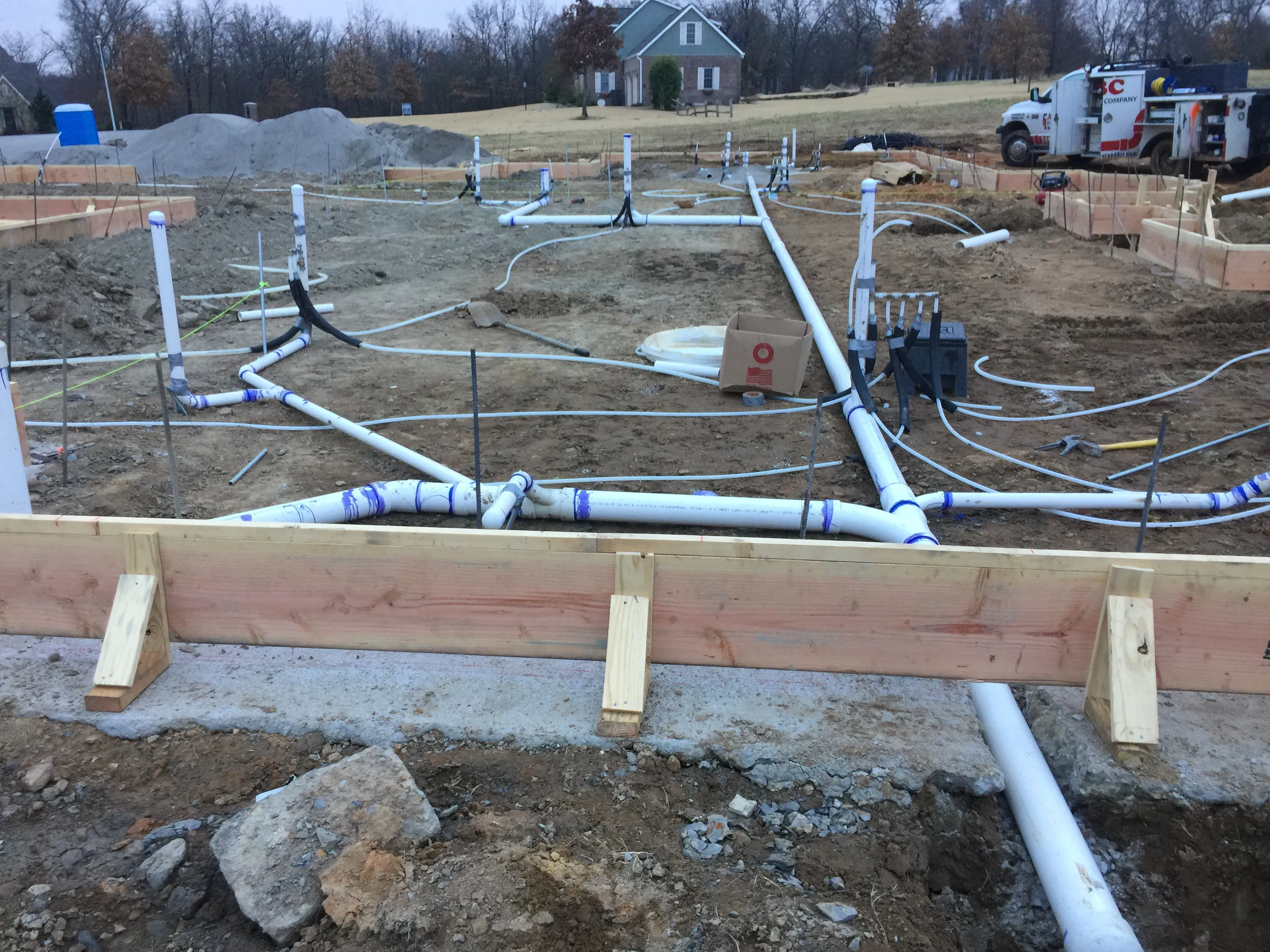 A large foundation plumbing rough-in at dusk with PVC drain and vent lines across the slab and ABC's truck in the background