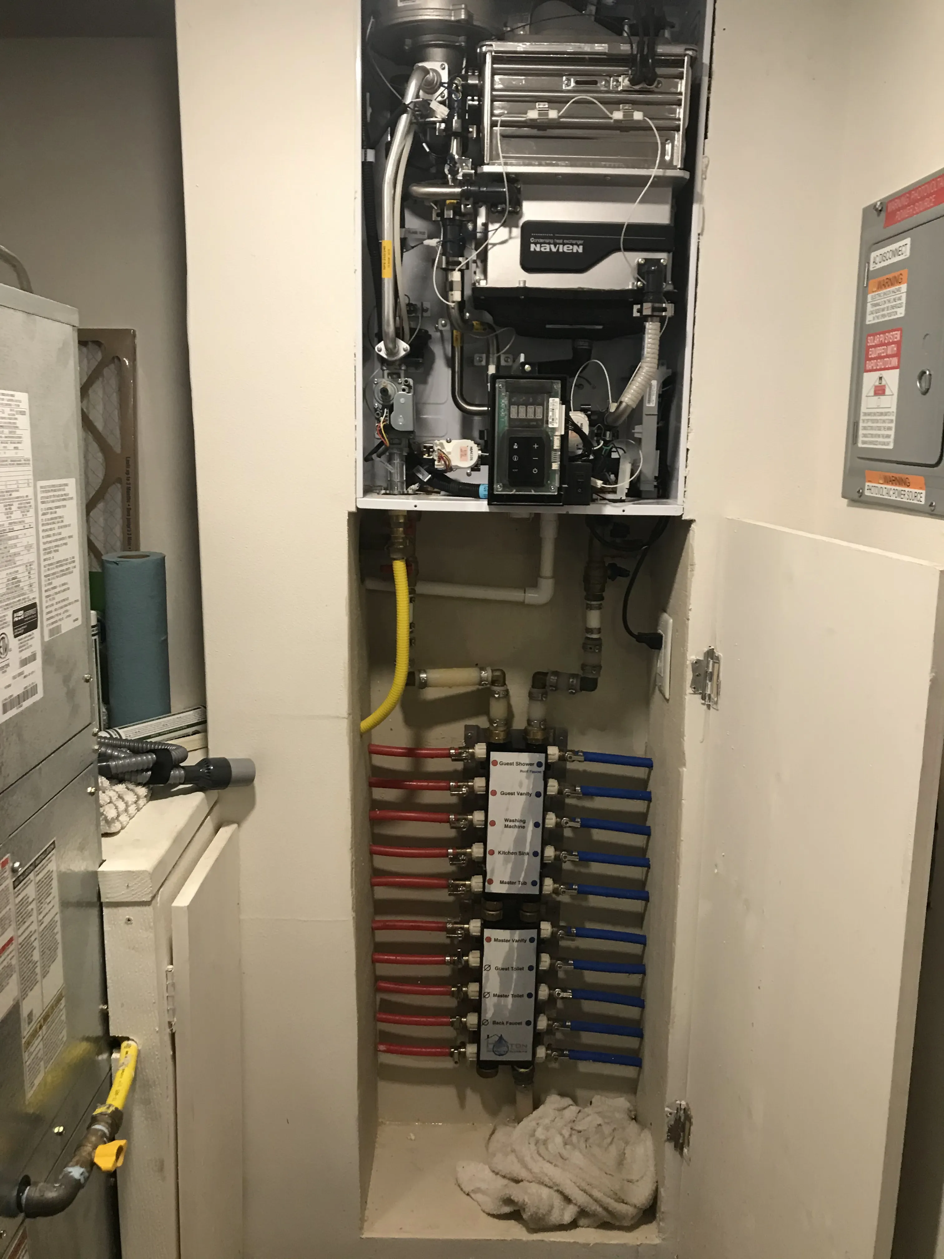 A Navien tankless water heater mounted above a PEX manifold with color-coded hot and cold lines