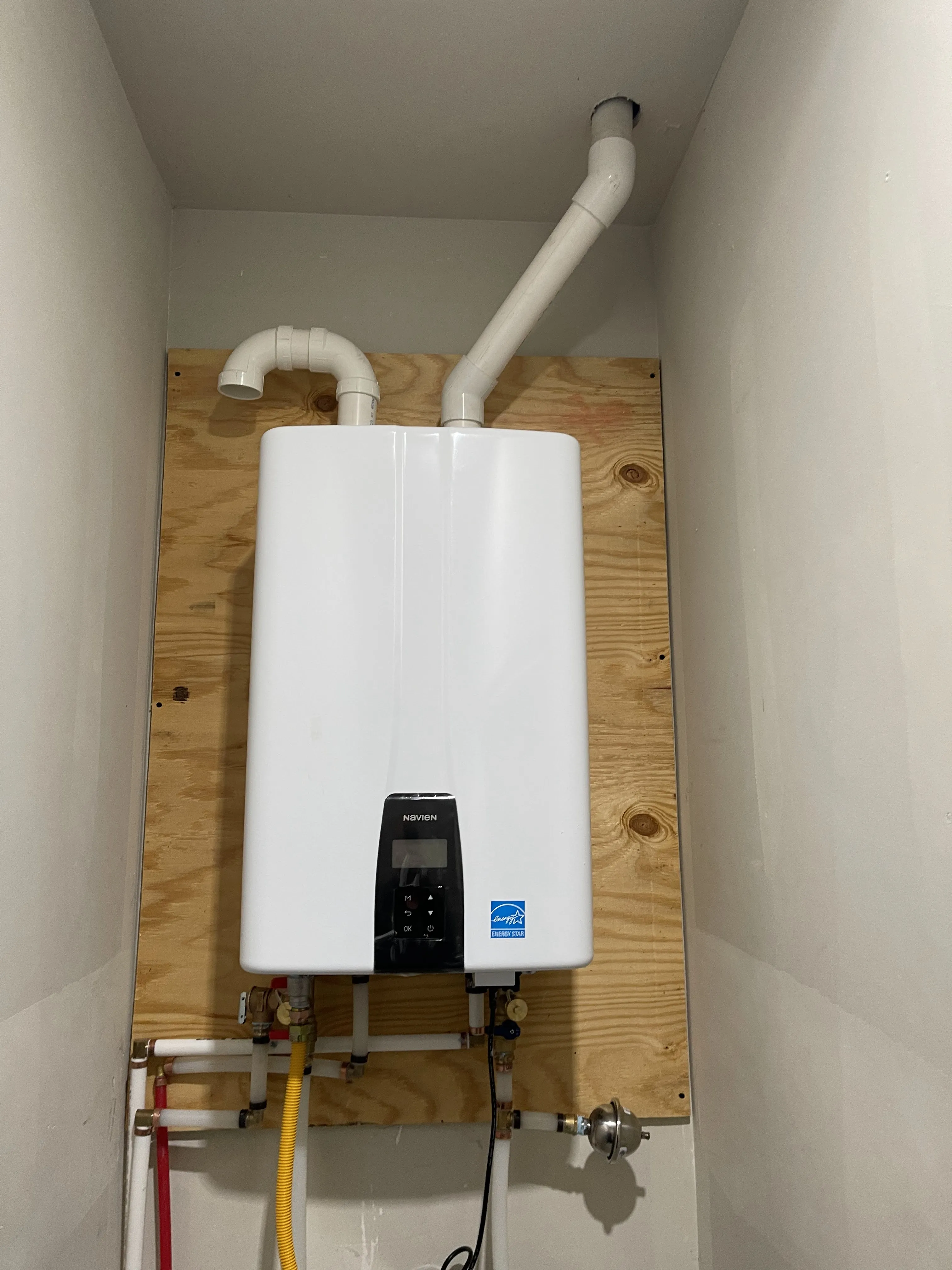 A Navien tankless water heater mounted on a plywood backer board with PVC venting