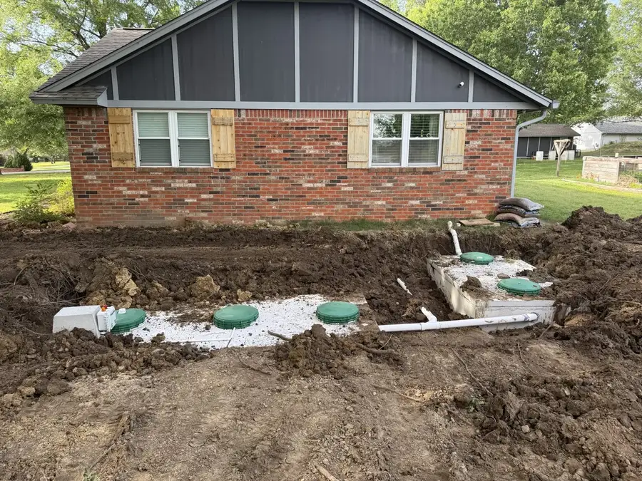 A new septic system going in beside a brick house, with green tank lids and white pipe in the dirt
