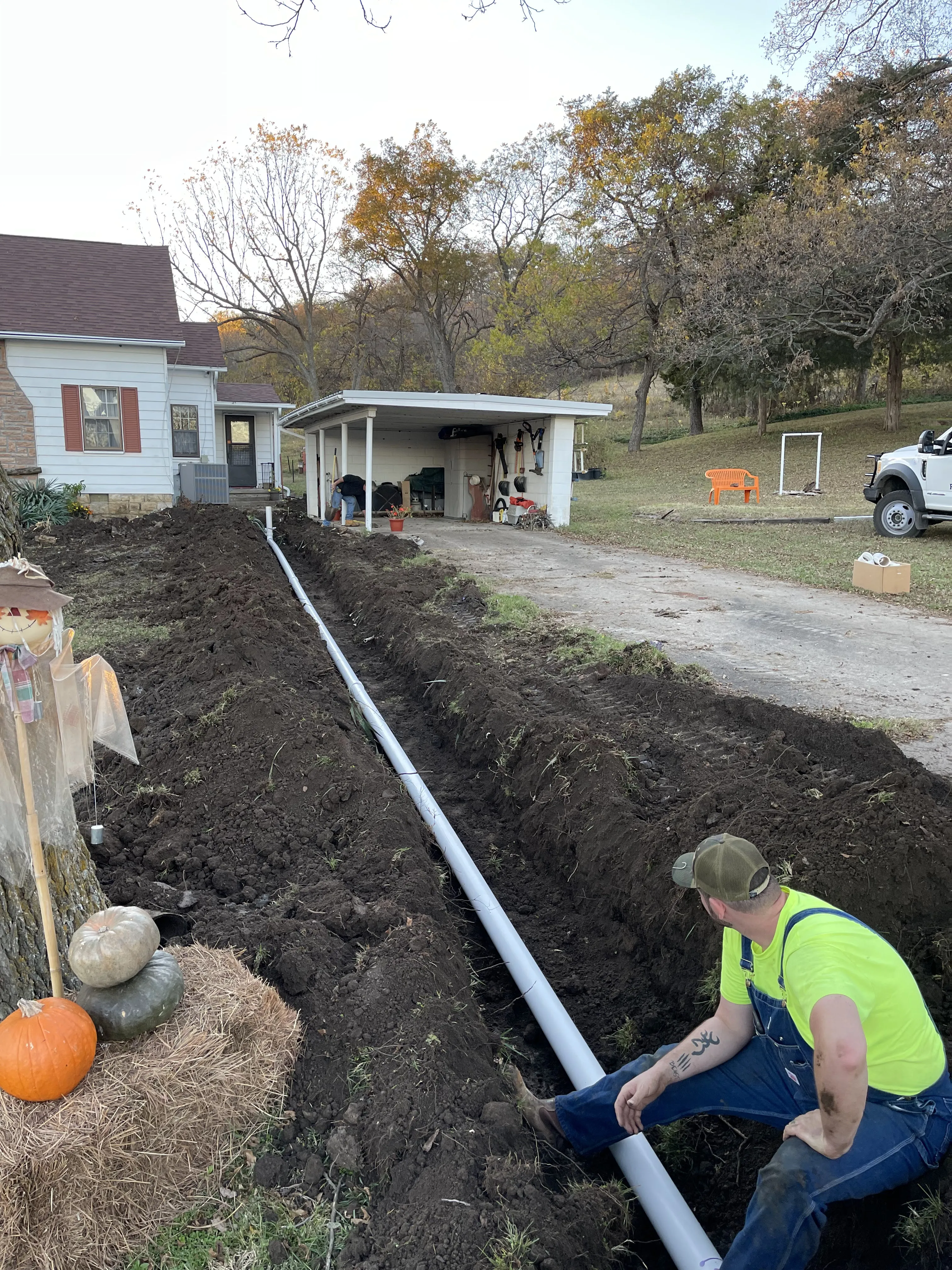 A crew member laying new PVC sewer pipe in a trench running to a house