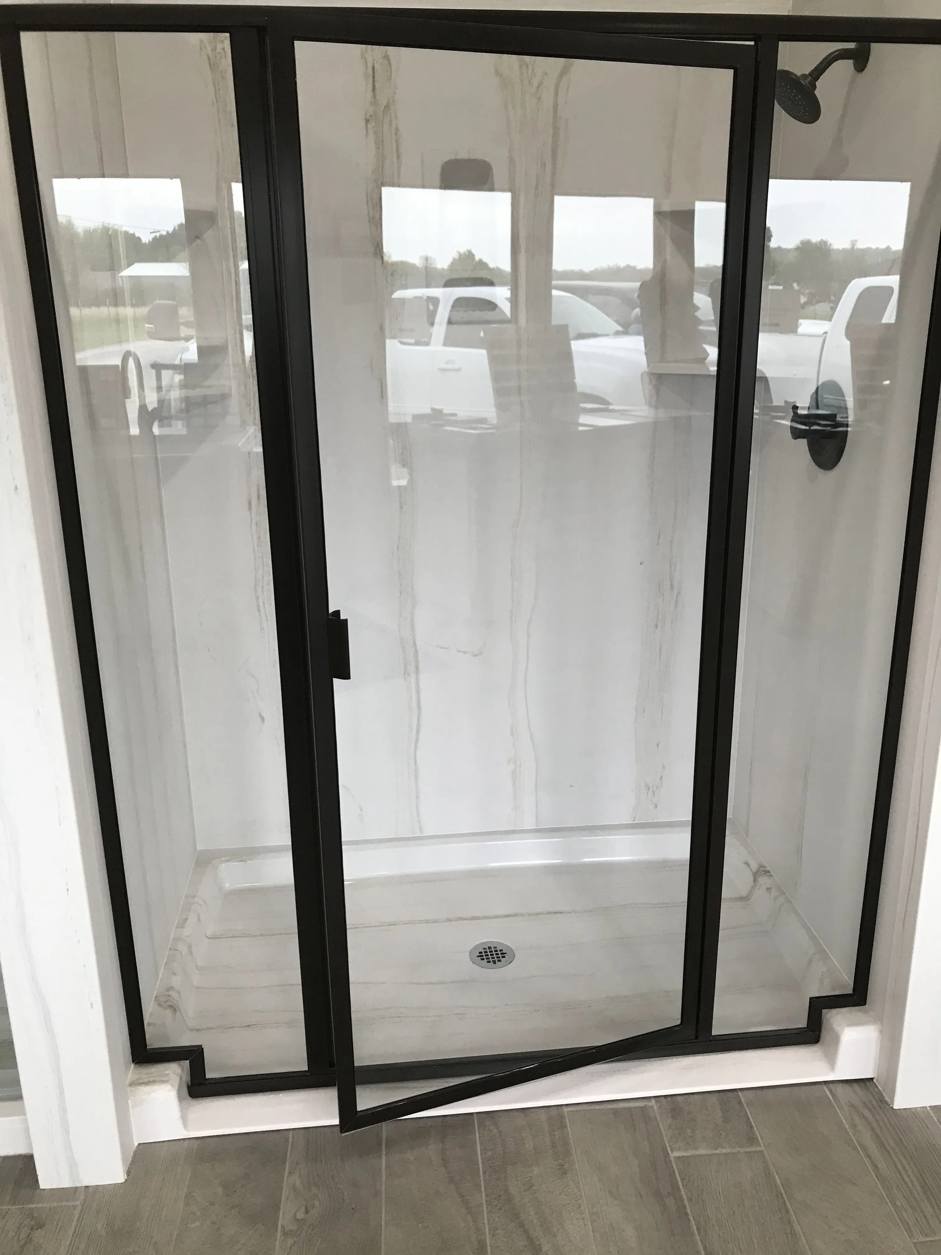 A glass shower enclosure with a black metal frame and marble-look wall panels