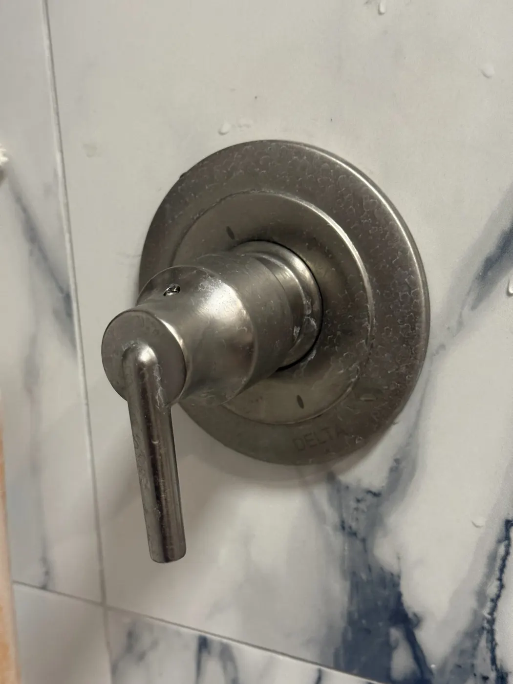 A brushed nickel shower valve trim on a white marble-look shower wall